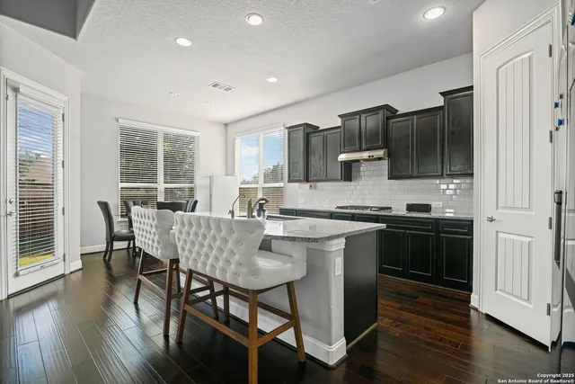 a kitchen with stainless steel appliances granite countertop a stove top oven a sink dishwasher a dining table and chairs with wooden floor