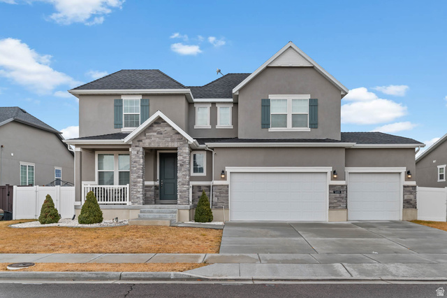 5686 Duke Lane Tooele, UT 84074 - Photo 3 of 38 View of front of house with stone siding, stucco siding, driveway, an attached garage, and covered porch