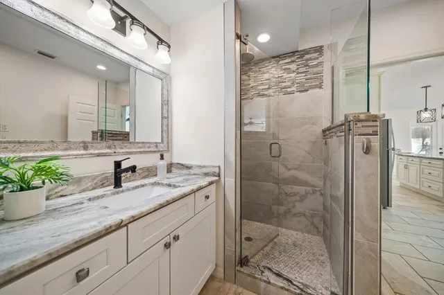 a bathroom with a granite countertop sink a mirror a glass door shower and vanity