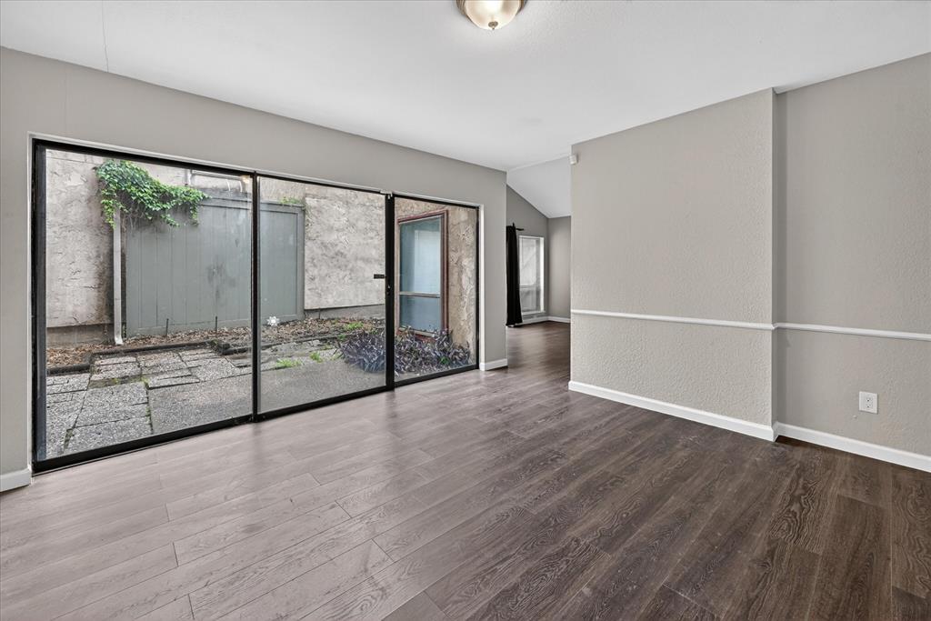 9809 Matchpoint Place Dallas, TX 75243 - Photo 3 of 21 Spacious interior featuring dark wood-finish flooring, a wall of sliding glass panels, and a contrasting light gray wall with decorative chair rail molding