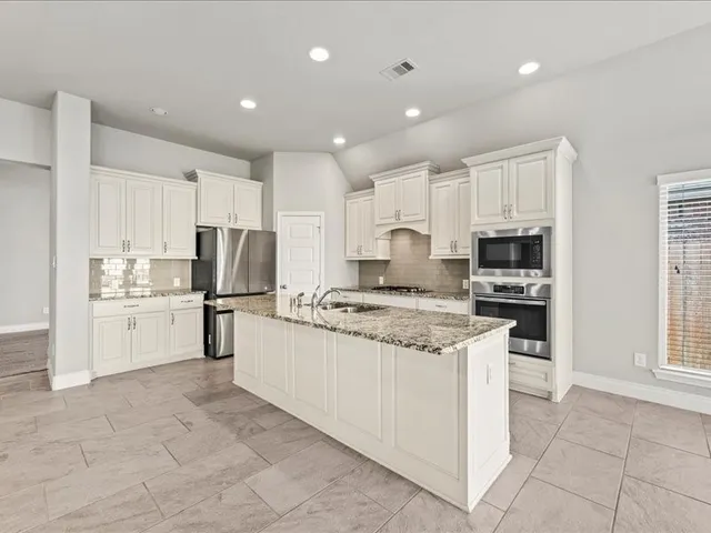 a kitchen with stainless steel appliances granite countertop a stove top oven a refrigerator a sink and white cabinets