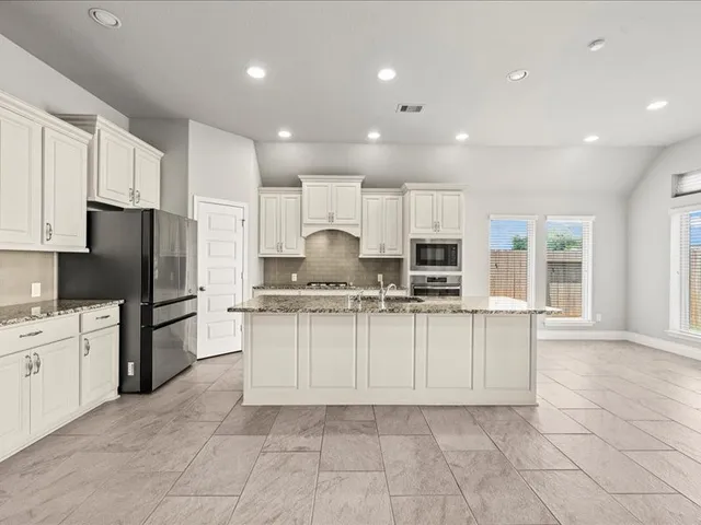 a kitchen with granite countertop a refrigerator and white cabinets