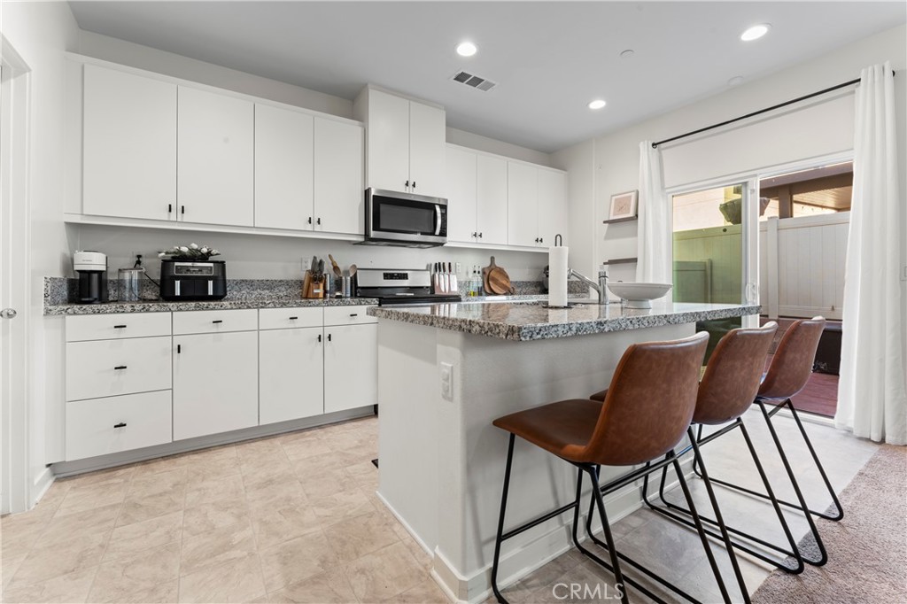 12704 Ironstone Way Moreno Valley, CA 92555 - Photo 25 of 38 a kitchen with stainless steel appliances granite countertop a stove a sink a refrigerator and white cabinets with wooden floor