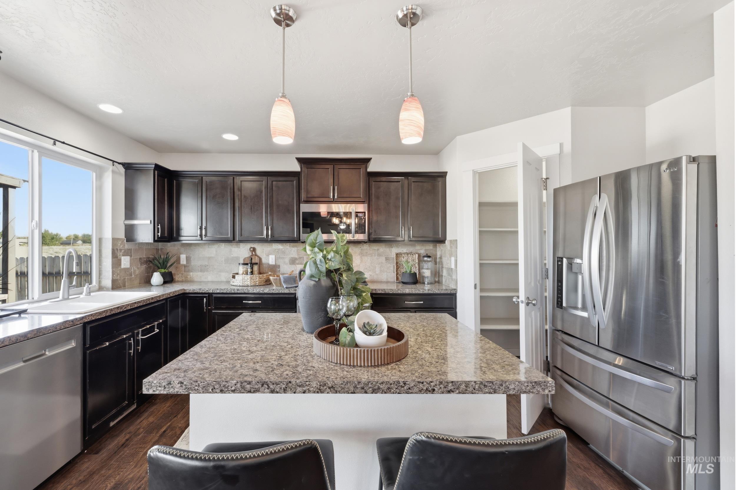 4855 South Chex Way Boise, ID 83709 - Photo 13 of 47 Kitchen featuring an expansive center island with a speckled countertop, dark wood-finish cabinetry, stainless steel appliances, a tile backsplash, and a pantry with built-in shelving