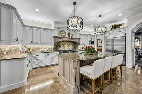 a kitchen with stainless steel appliances granite countertop a stove a sink a refrigerator a center island a dining table and chairs