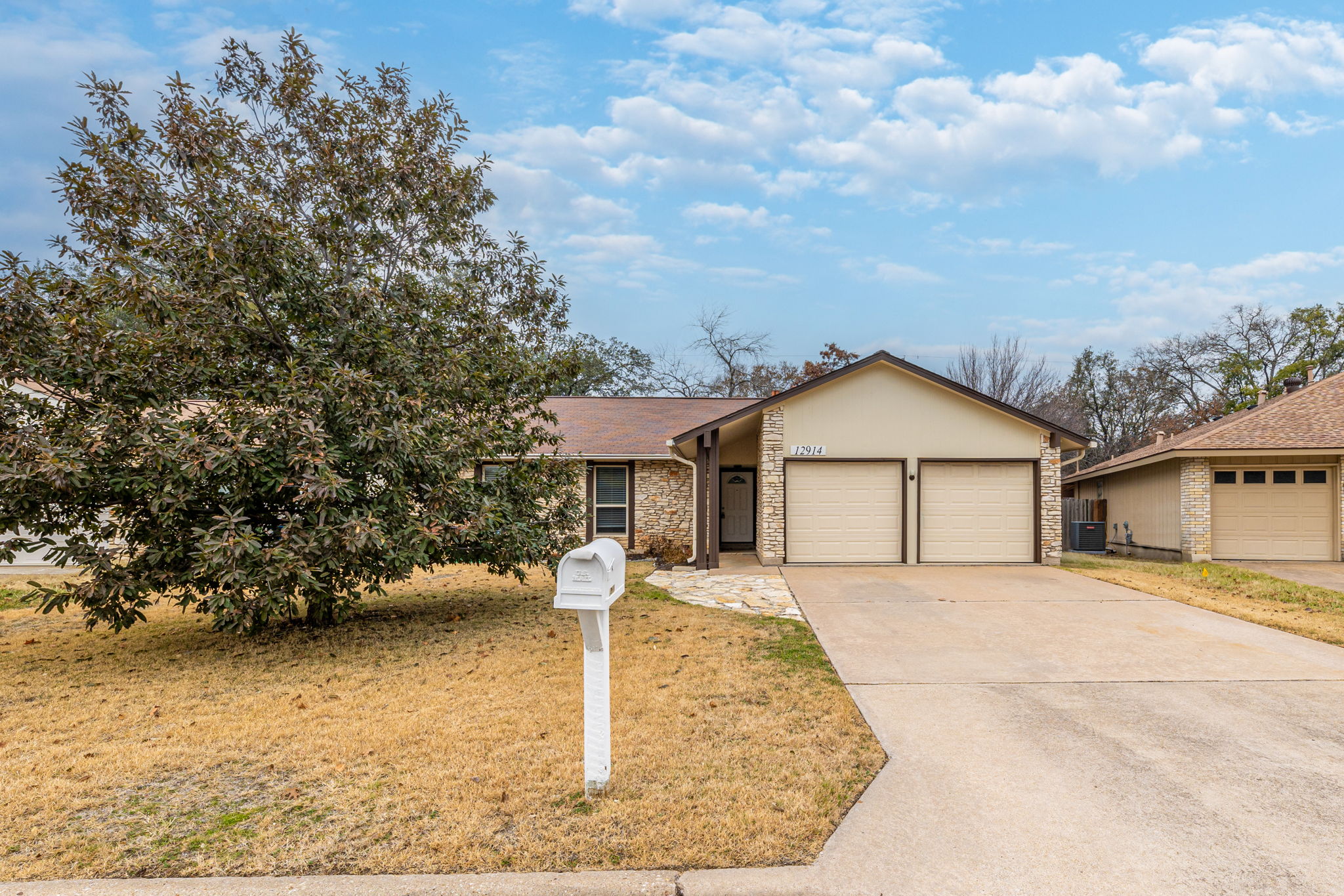 Single story home featuring driveway, a garage, a front lawn, stone siding, and stucco siding