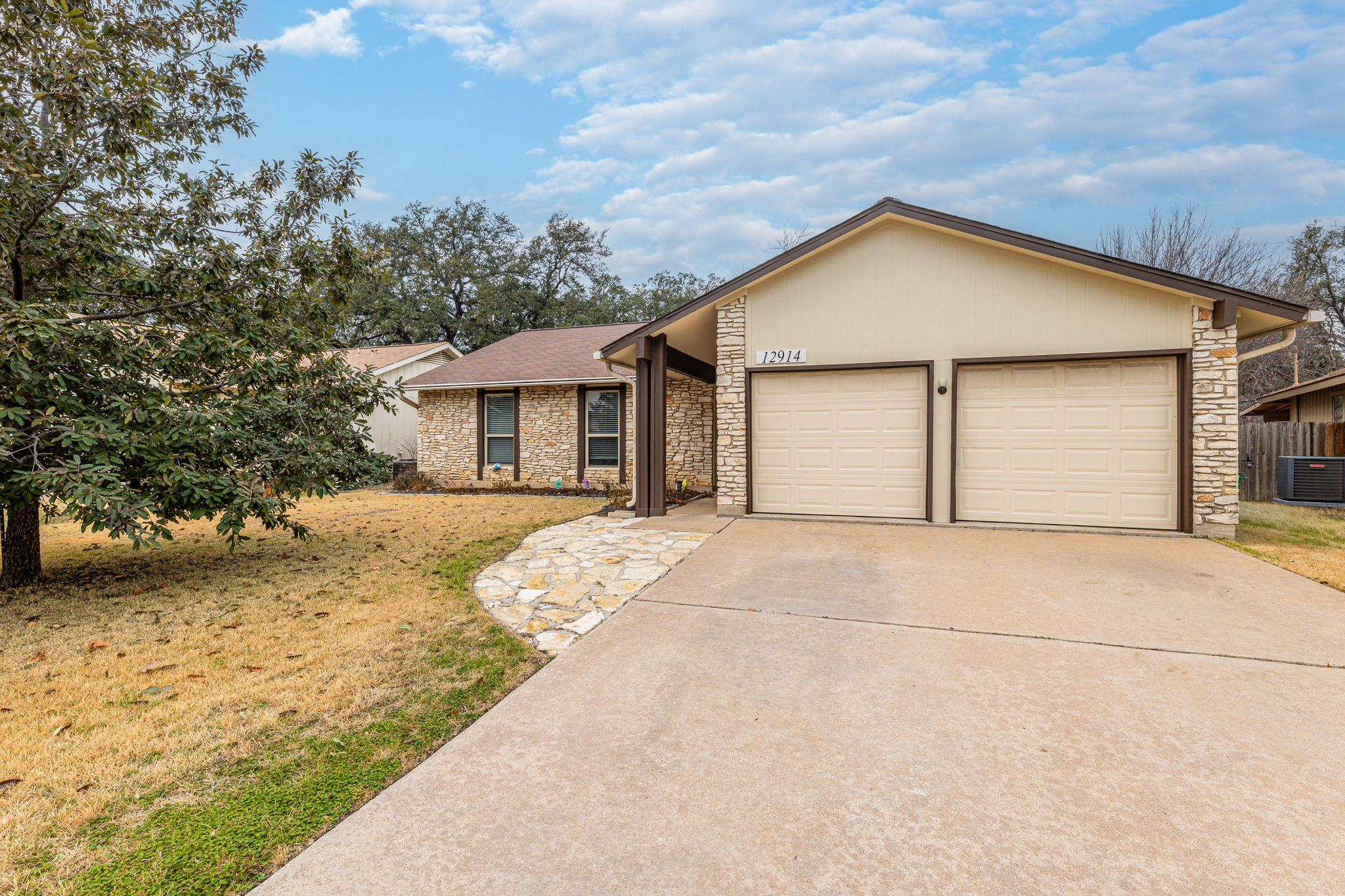 12914 Pegasus Street Austin, TX 78727 - Photo 2 of 30 View of front of house featuring stone siding, driveway, a front lawn, and a garage
