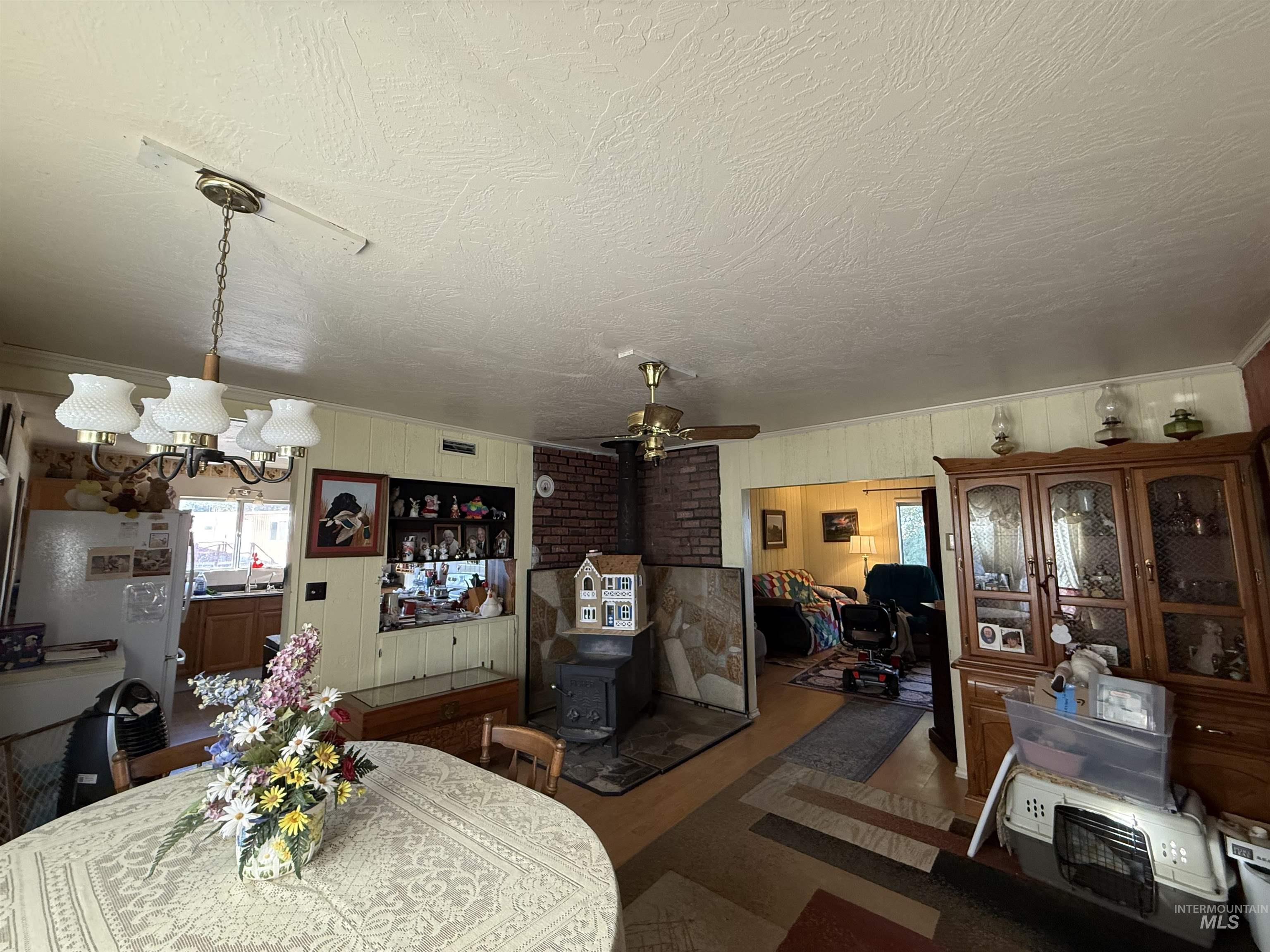 19241 West Homedale Road Caldwell, ID 83607 - Photo 23 of 35 Dining area featuring a ceiling fan, a wood stove, a chandelier, wood walls, and dark wood-type flooring