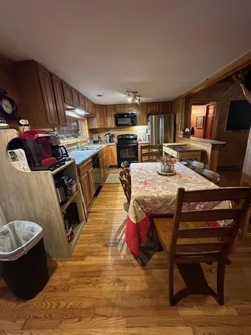 a kitchen with stainless steel appliances granite countertop a stove top oven a sink a dining table and chairs with wooden floor