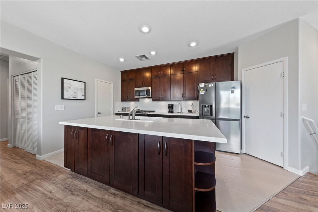 9121 Ripple Ridge Avenue, Unit 101 Las Vegas, NV 89149 - Photo 3 of 16 Kitchen with stainless steel appliances, backsplash, dark brown cabinets, light countertops, and light wood-type flooring