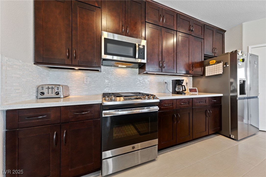 9121 Ripple Ridge Avenue, Unit 101 Las Vegas, NV 89149 - Photo 4 of 16 Kitchen featuring stainless steel appliances, decorative backsplash, light countertops, dark brown cabinetry, and light tile patterned floors