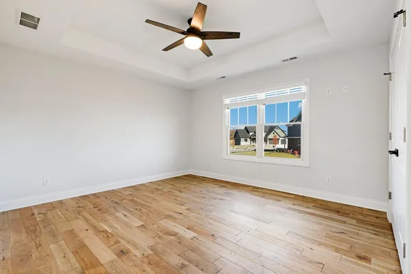 an empty room with wooden floor fan and windows