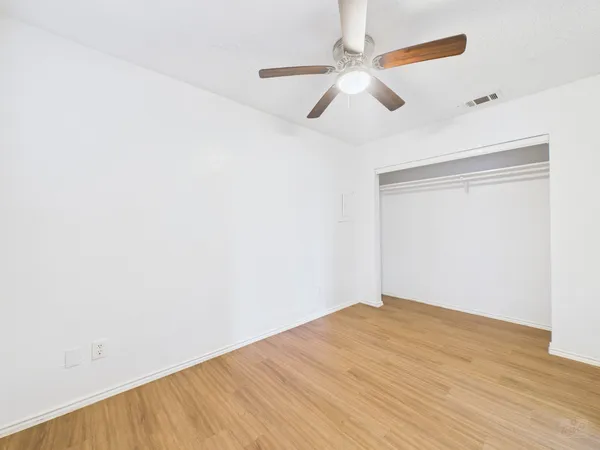 an empty room with wooden floor fan and windows