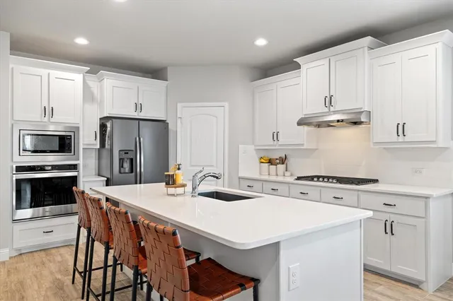 a kitchen with stainless steel appliances a stove a sink a refrigerator and white cabinets