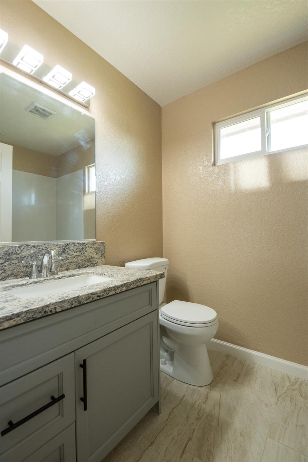 1621 Davis Street Ripon, CA 95366 - Photo 25 of 43 a bathroom with a granite countertop sink a toilet and a mirror