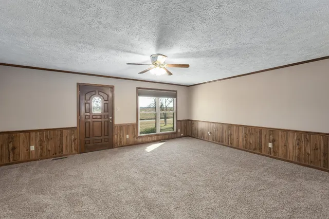 an empty room with chandelier fan and windows