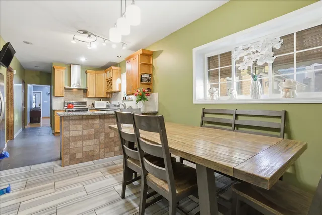 a dining room with stainless steel appliances kitchen island granite countertop a table chairs and a refrigerator