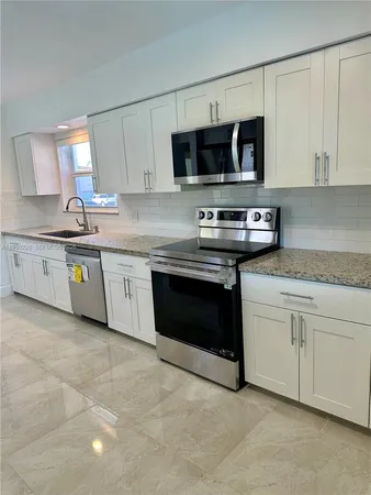 a kitchen with stainless steel appliances granite countertop white cabinets a microwave a sink and a counter
