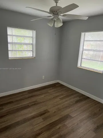 an empty room with wooden floor fan and windows