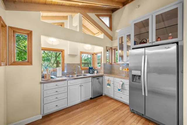 a kitchen with stainless steel appliances granite countertop a refrigerator a sink dishwasher a stove with white cabinets and wooden floor