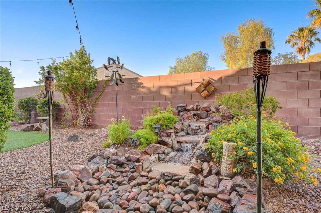 1604 Cattle Ranch Place Henderson, NV 89002 - Photo 71 of 99 A tranquil backyard oasis features a rock waterfall, lush landscaping, and festive string lights.