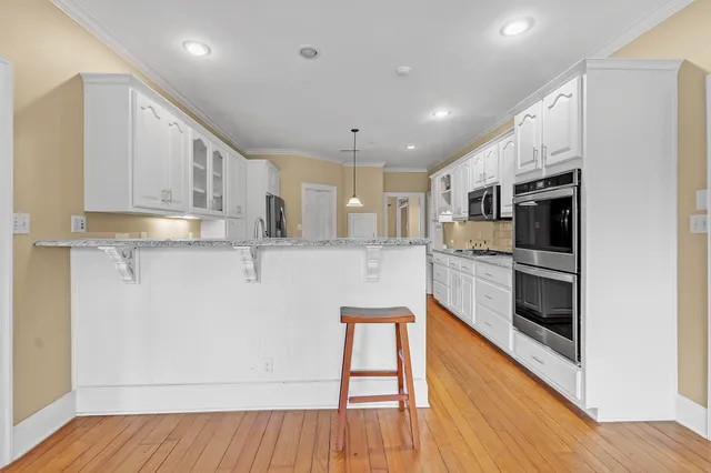 a kitchen with stainless steel appliances kitchen island granite countertop a stove a sink and white cabinets with wooden floor