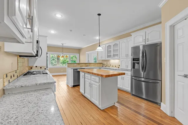 a kitchen with stainless steel appliances granite countertop a refrigerator a sink dishwasher a stove and white countertops with wooden floor