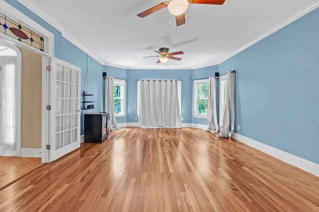 an empty room with wooden floor chandelier fan and windows