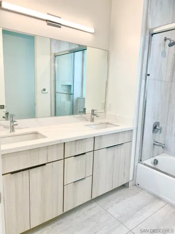 a bathroom with a double vanity sink a large mirror and a bathtub