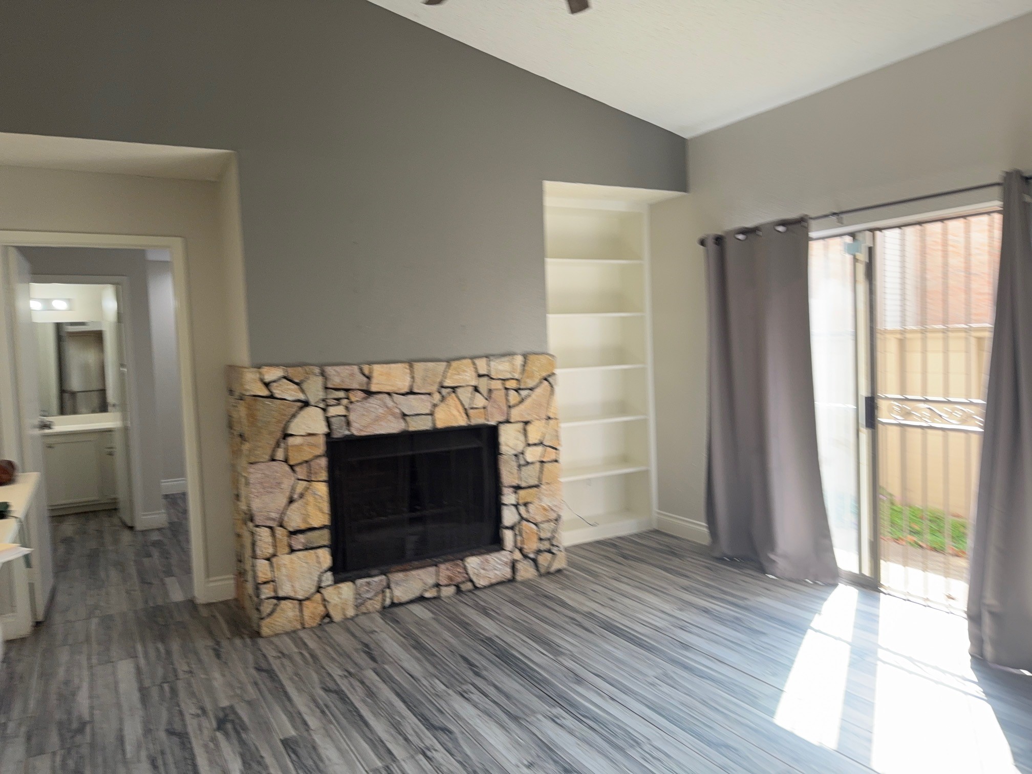a view of an empty room with wooden floor fireplace and a window