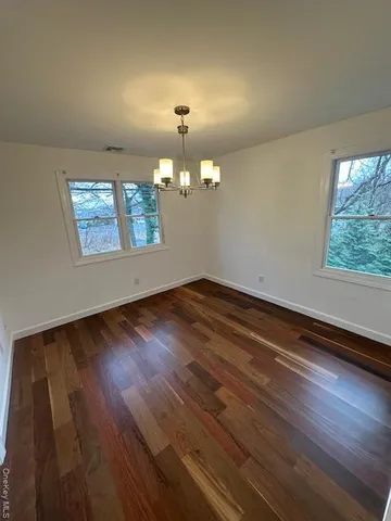 an empty room with wooden floor chandelier and windows