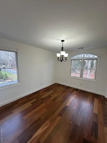 an empty room with wooden floor chandelier and windows