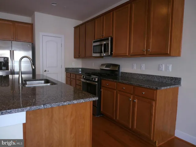 a kitchen with stainless steel appliances granite countertop a stove a sink dishwasher and a microwave oven with wooden cabinets