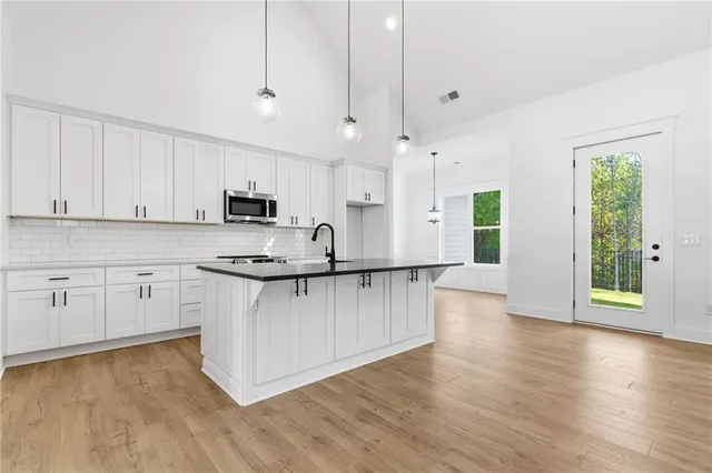 a kitchen with stainless steel appliances granite countertop a stove a sink and white cabinets with wooden floor