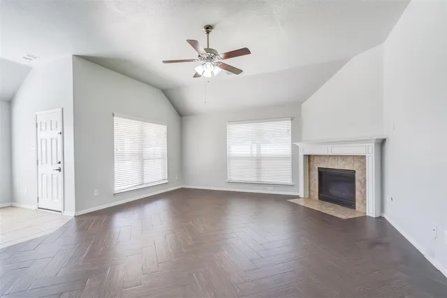 an empty room with wooden floor fireplace and windows