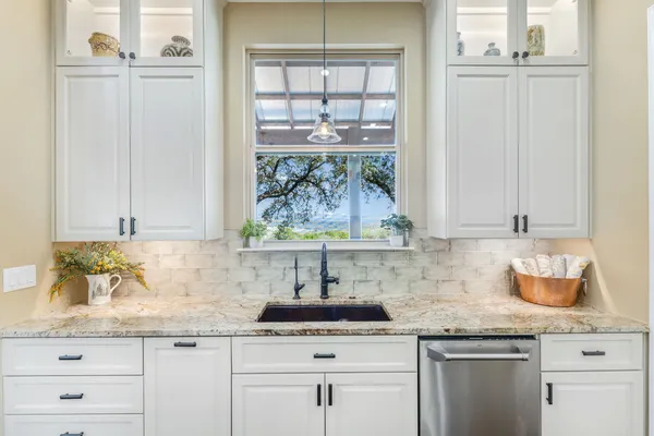 a sink with granite countertop white cabinets and a window