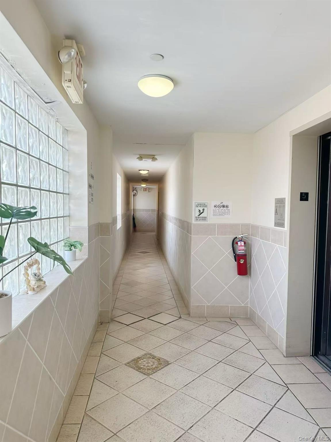46-06 88th Street, Unit 5B Queens, NY 11373 - Photo 3 of 11 Hall with light tile patterned floors, tile walls, elevator, and wainscoting