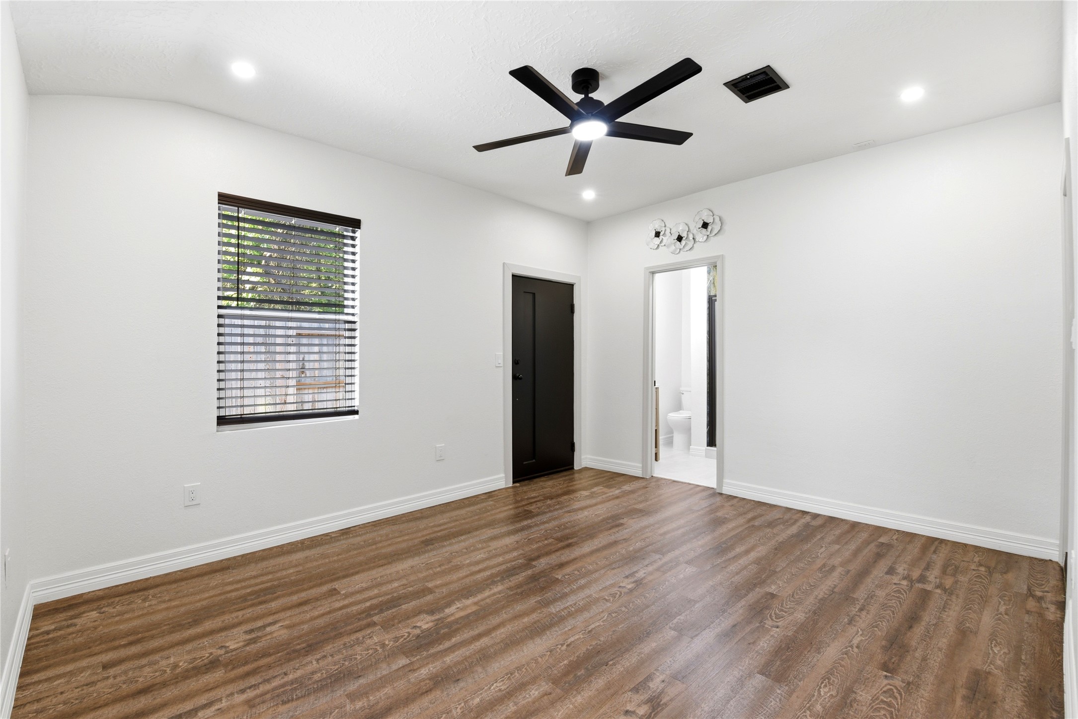 9403 Spaulding Street Houston, TX 77016 - Photo 33 of 50 This room features hardwood flooring, a ceiling fan, and recessed lighting. A window with blinds provides natural light. There's an adjacent bathroom with modern fixtures, perfect for convenience and comfort.