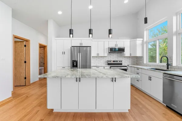 a kitchen with stainless steel appliances granite countertop a stove a sink a refrigerator and white cabinets with wooden floor