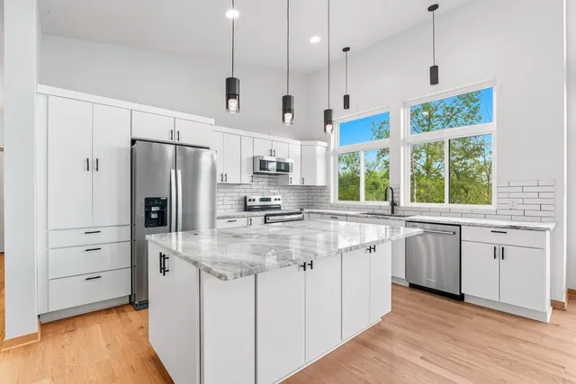 a kitchen with stainless steel appliances granite countertop a refrigerator a stove and white cabinets with wooden floors