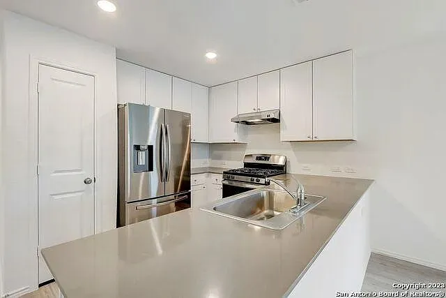 a kitchen with stainless steel appliances granite countertop a refrigerator a sink a stove and white cabinets