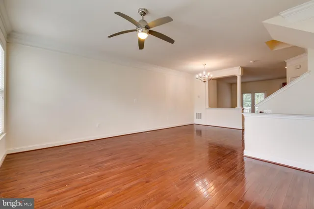 a view of an empty room with wooden floor and a ceiling fan
