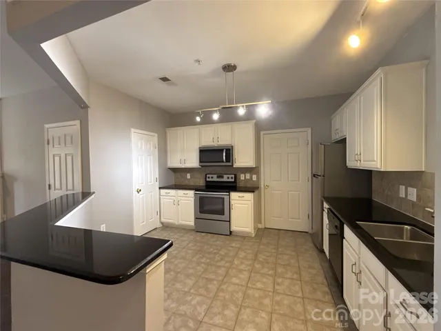 a kitchen with granite countertop a sink a stove top oven a refrigerator and cabinets