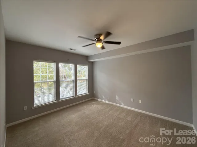 an empty room with chandelier fan and windows