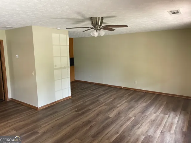 an empty room with wooden floor a ceiling fan and windows
