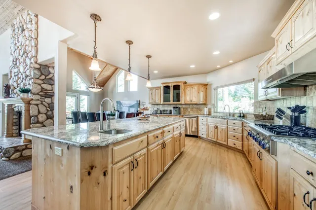 a kitchen with stainless steel appliances granite countertop a stove a refrigerator a sink a dining table and chairs with wooden floor