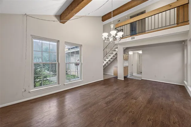 an empty room with wooden floor chandelier and windows