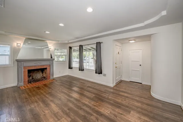 a view of an empty room with wooden floor fireplace and a window