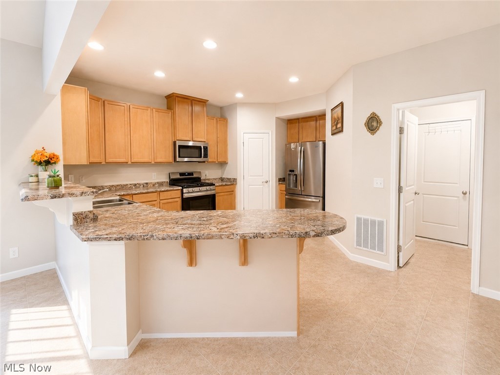 867 Starr Ridge Street Southeast Massillon, OH 44646 - Photo 10 of 29 Open-concept kitchen featuring wood cabinetry, stainless steel appliances, and a breakfast bar with stone-finish countertops