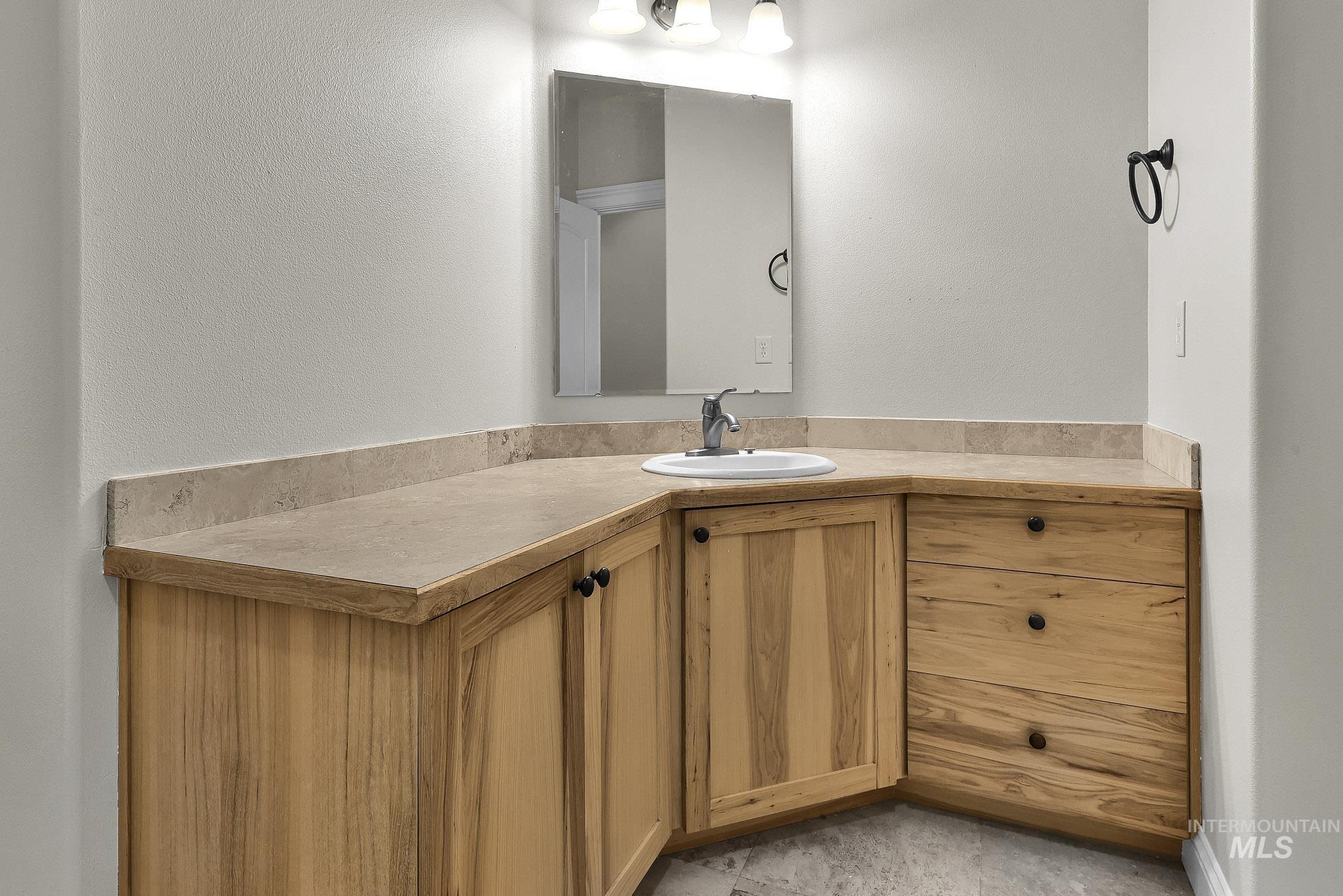 2172 West Cedar Grove Street Meridian, ID 83646 - Photo 30 of 49 Corner vanity with a light wood-finish cabinetry, a single basin sink, a neutral-toned countertop with backsplash, a wall-mounted mirror, and overhead lighting